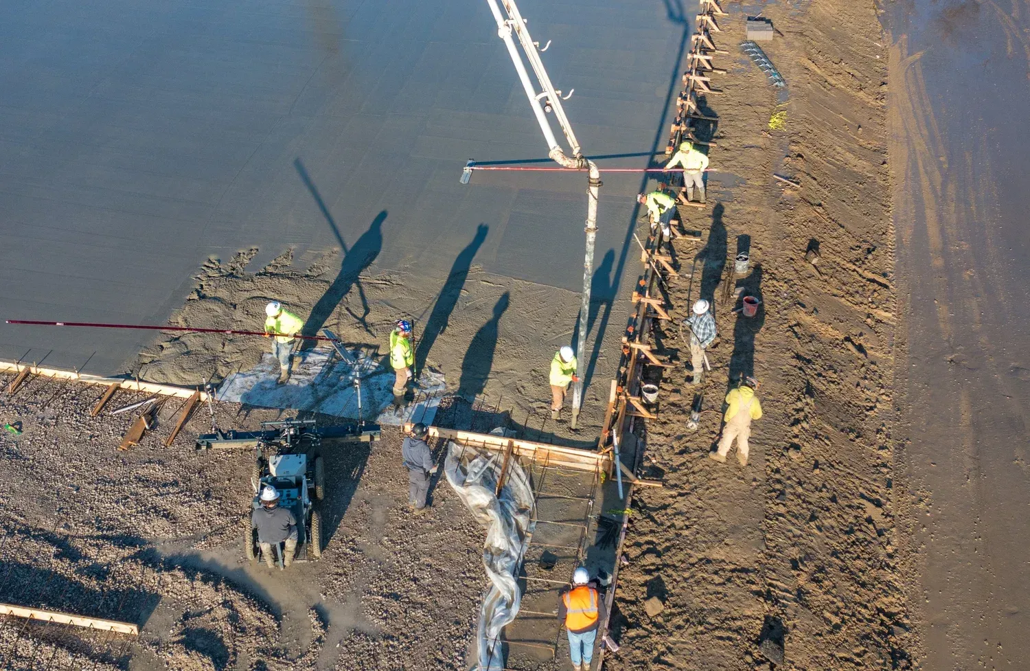 Workers install a large pipeline on a muddy construction site beside a road