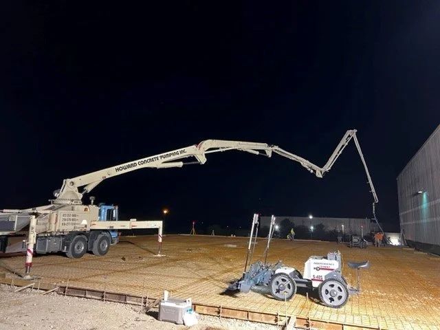 Concrete pump truck at night pouring concrete at a construction site beside a building