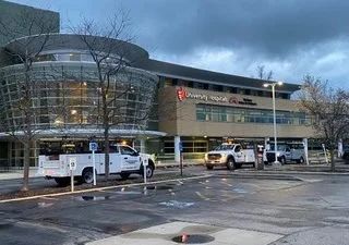 Rainy exterior of a modern glass building with parked utility trucks and wet pavement.
