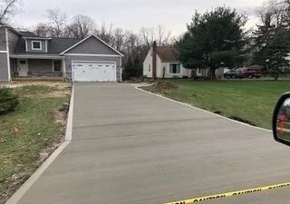 Freshly poured concrete driveway leading to a gray house with a white garage door and yard on both sides