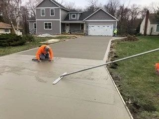 Worker smoothing fresh concrete driveway in front of a gray house on a cloudy day