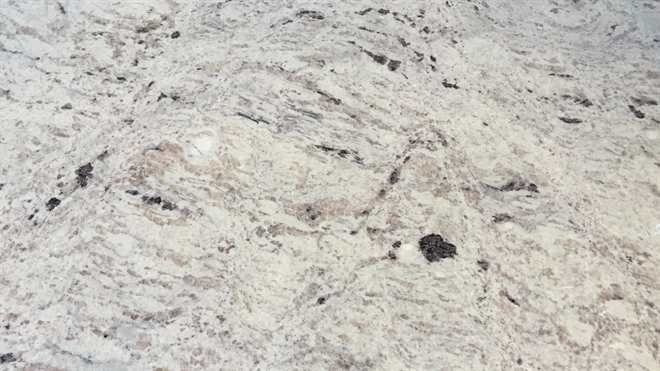 A close up of a white granite counter top with black spots.