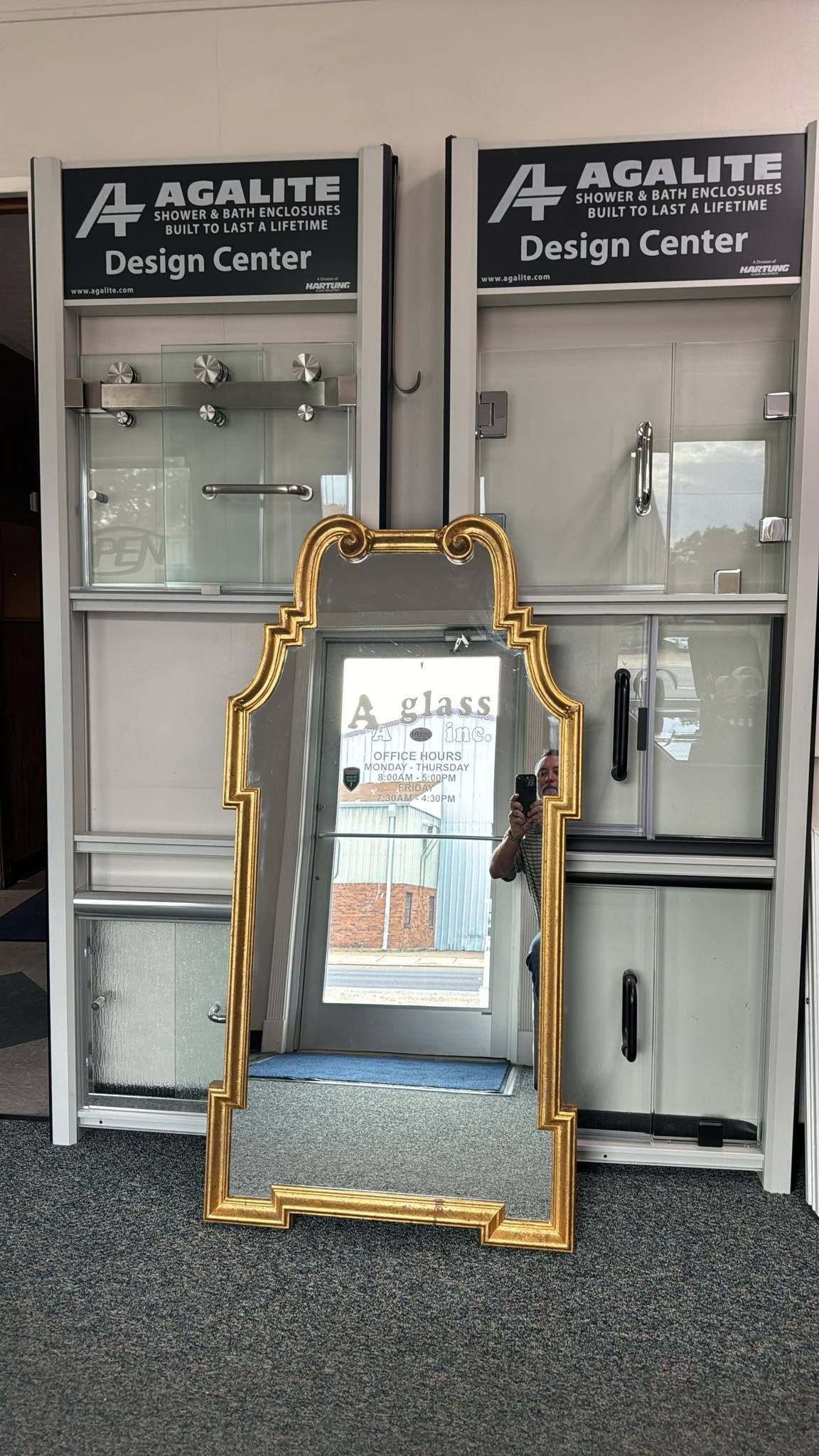 Gold-framed mirror leaning in front of glass cabinets labeled “A-Quality Design Center”