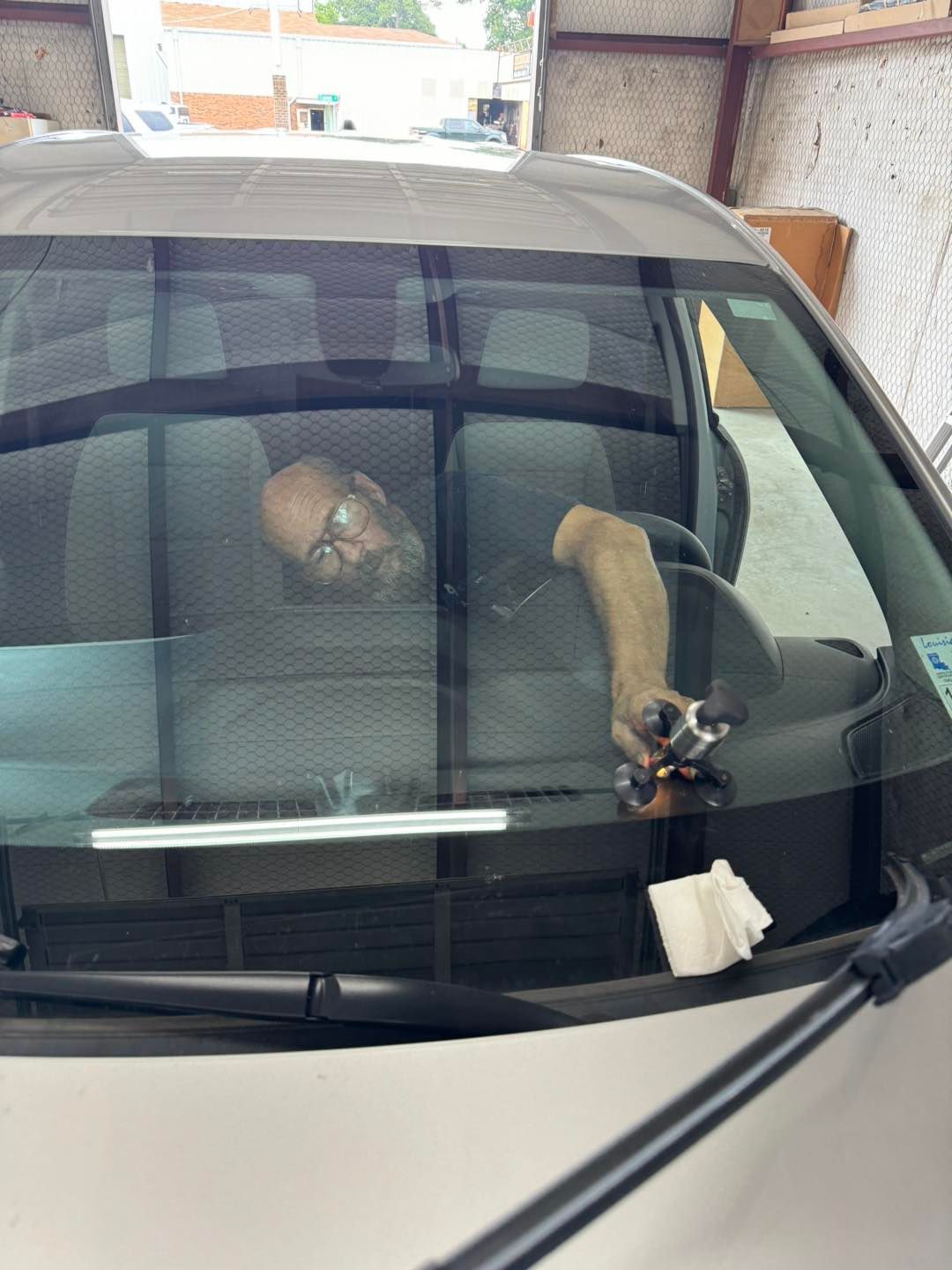 Dog resting on the rear window shelf of a car, seen through the windshield.