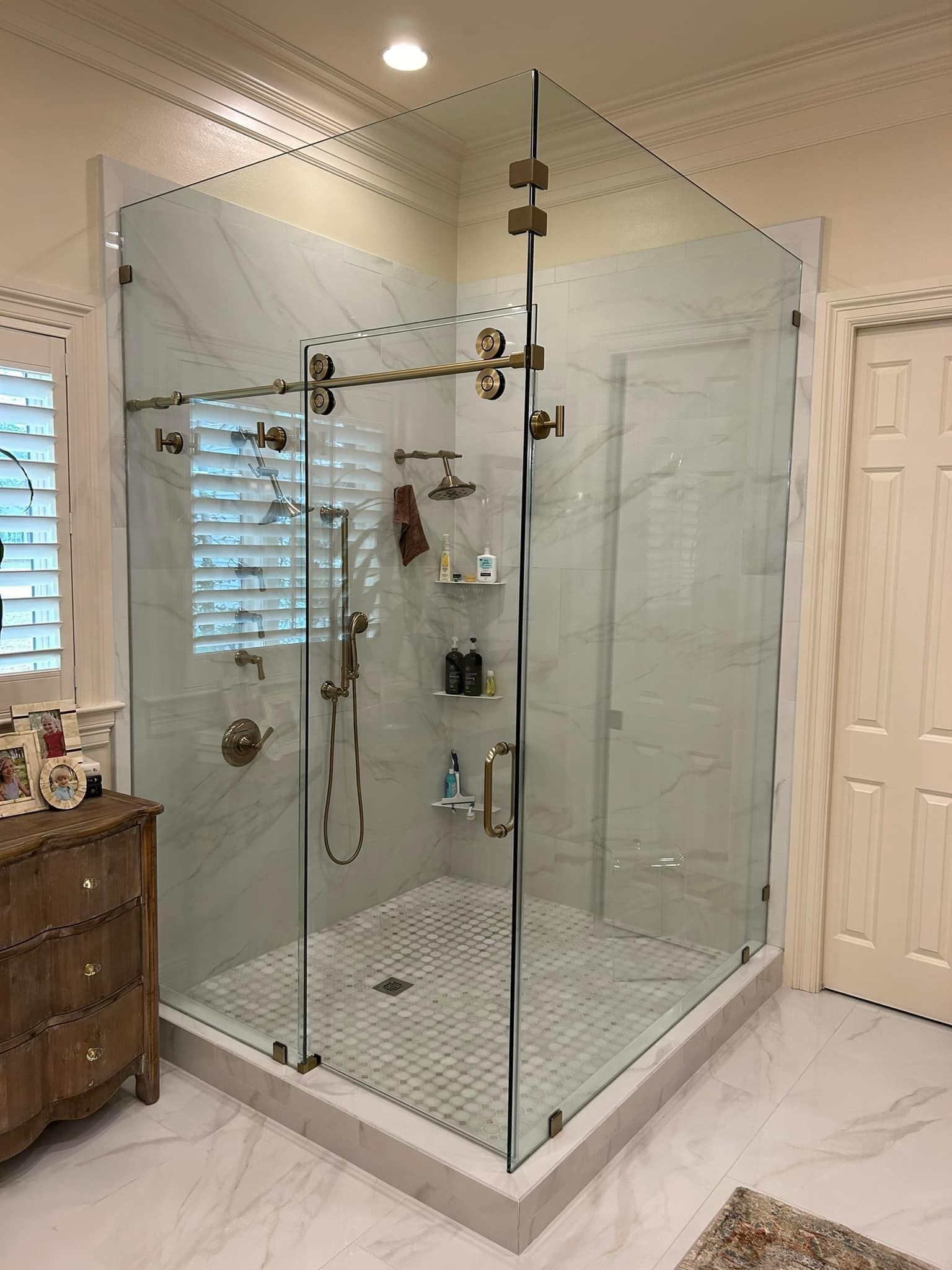 Glass walk-in shower with brass fixtures in a bright tiled bathroom