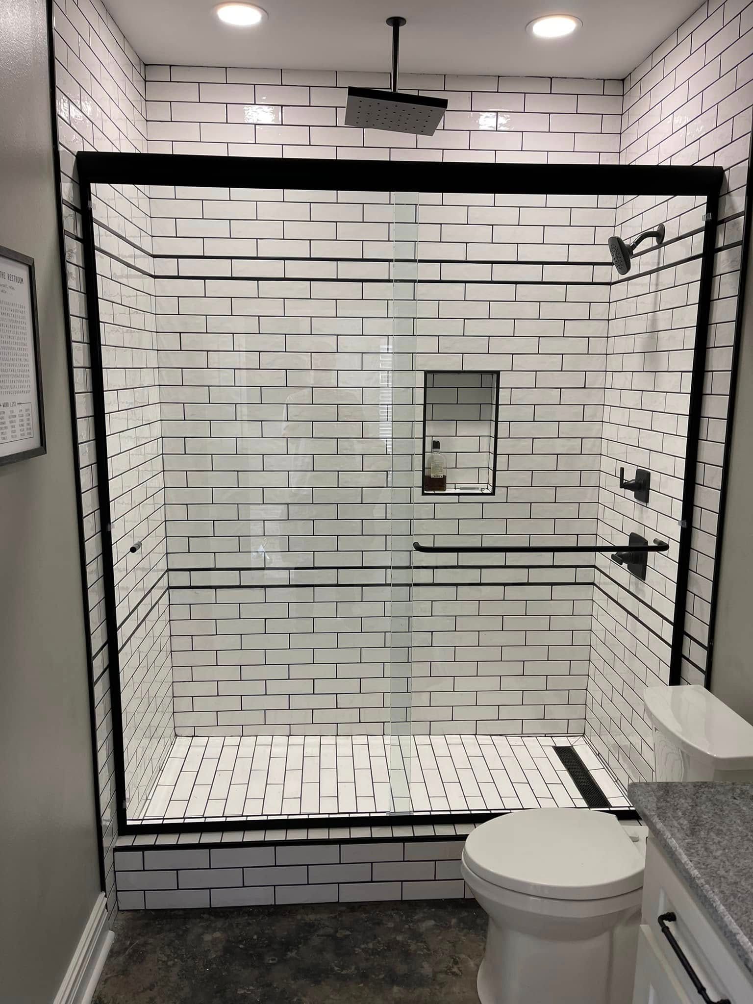 Modern bathroom with white subway-tile shower, glass door, grab bar, and toilet in foreground