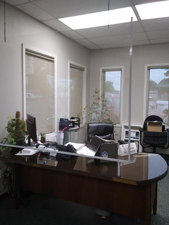 Empty office with a large wooden desk, computer monitor, chairs, and windows along the back wall.