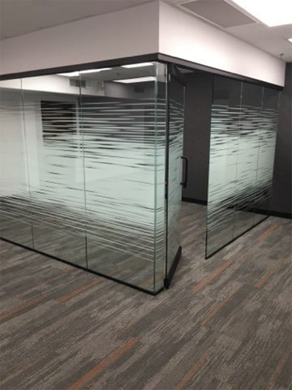 Glass office partition with frosted horizontal stripes in a carpeted interior hallway