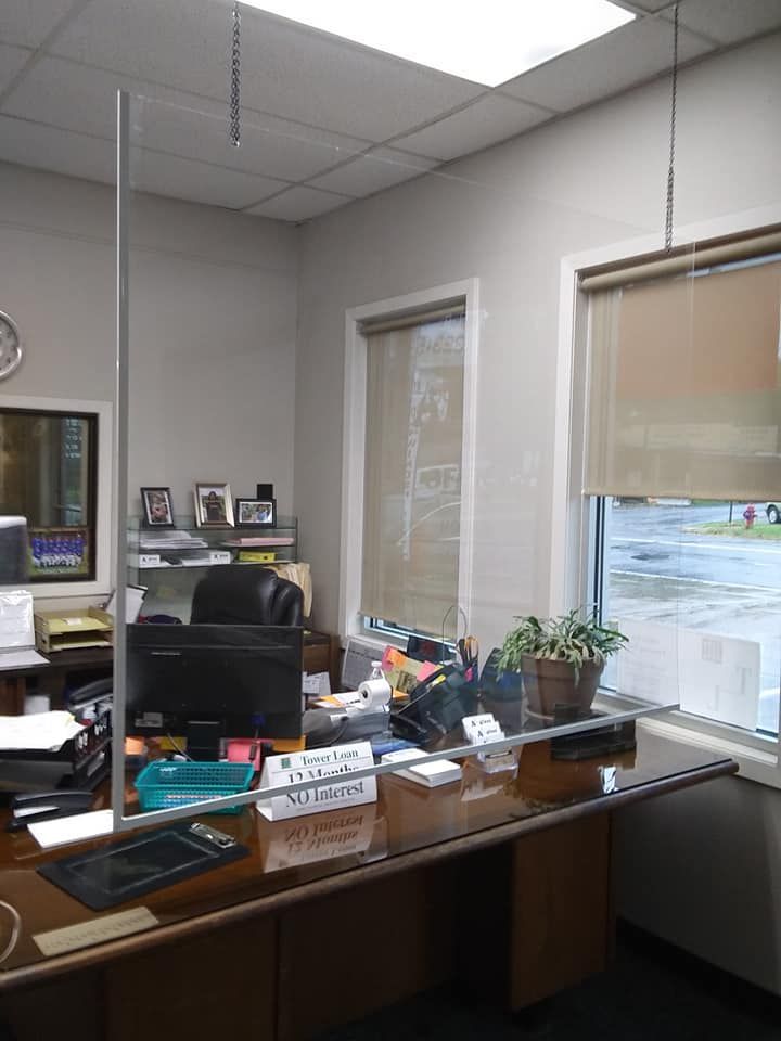 Office desk by windows with computer, paperwork, and potted plants in a corner office.