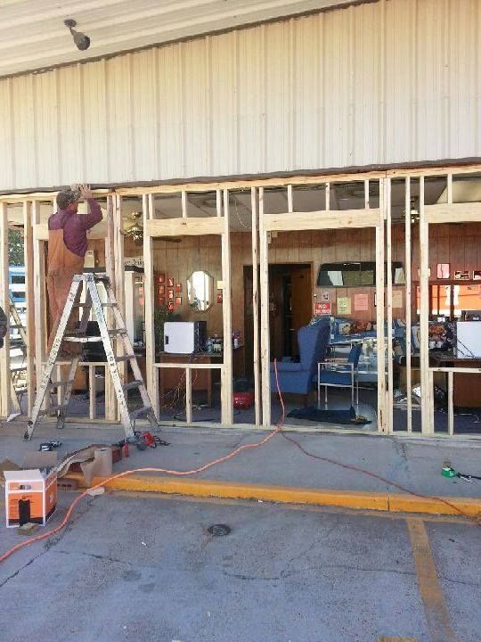 Construction crew framing a storefront opening with ladders and tools outside a beige building