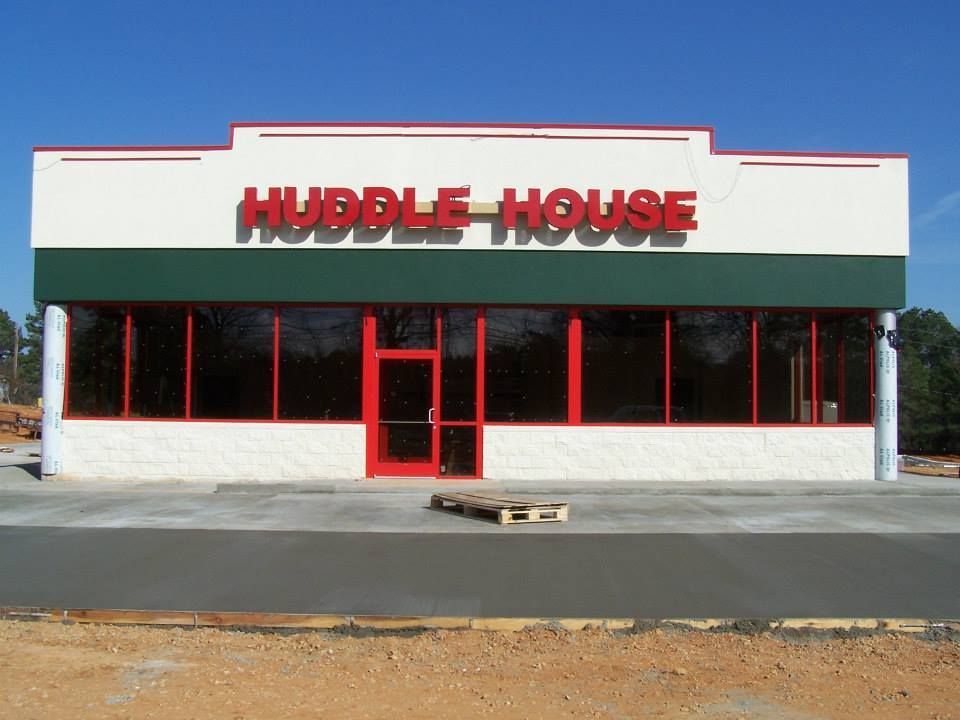 Front view of a Huddle House restaurant with red signage and a red entrance on a plain lot