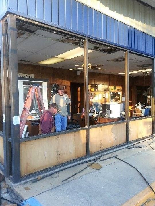 Storefront with large windows; two people inside near clothing racks and a brightly lit interior.