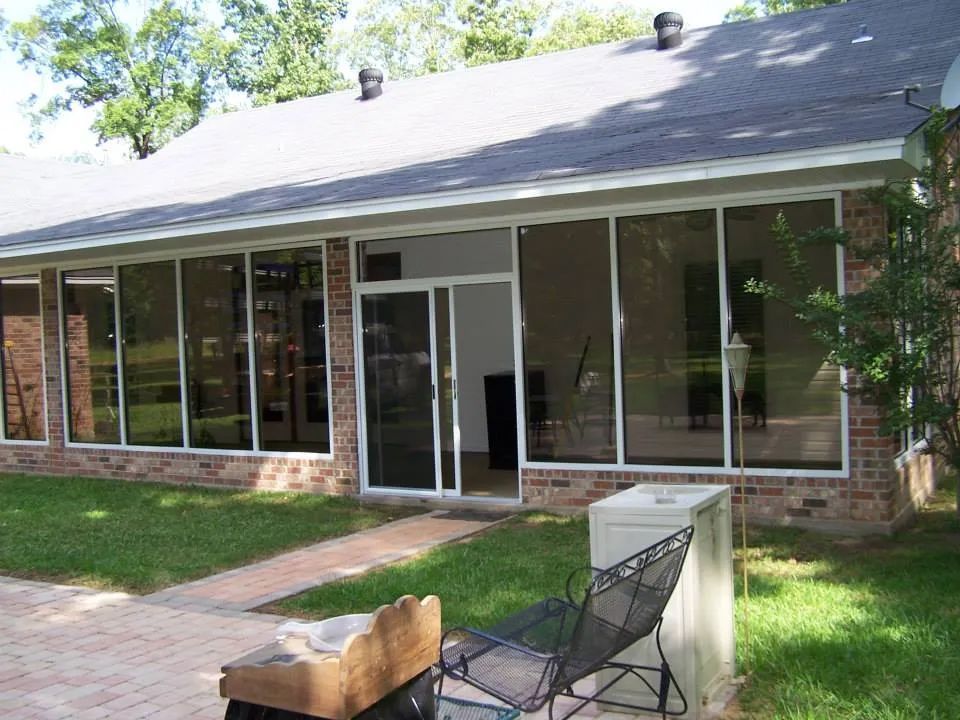 Brick house with large windows, screened porch, and patio chairs on a brick walkway