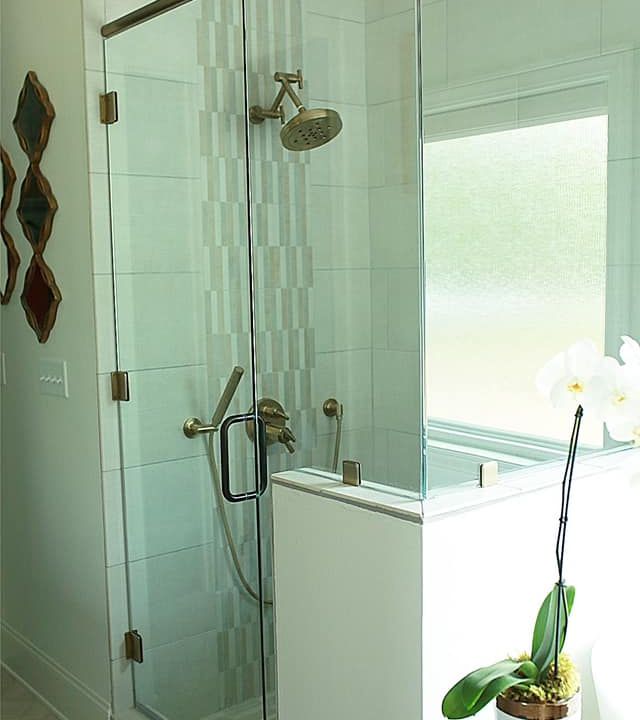 Glass shower with chrome fixtures beside a frosted window and white orchid on the ledge