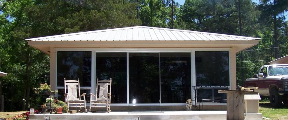 Small white house with a covered porch, large windows, patio chairs, and trees in front