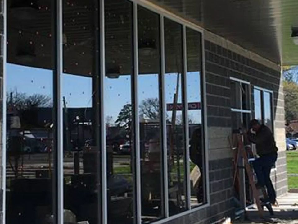 Two people working on a storefront window with a ladder outside a brick building