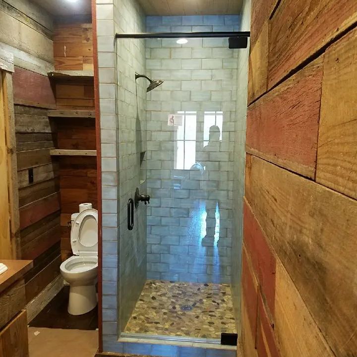 Small bathroom with a glass shower stall, wood-paneled walls, and a toilet beside the shower.