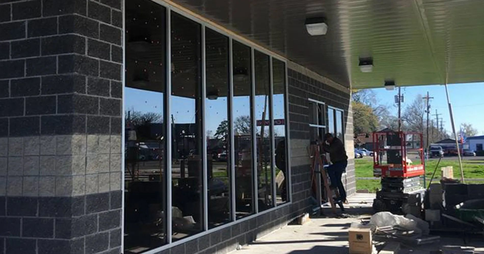 Storefront with large windows; two workers outside under an overhang near boxes and construction materials.