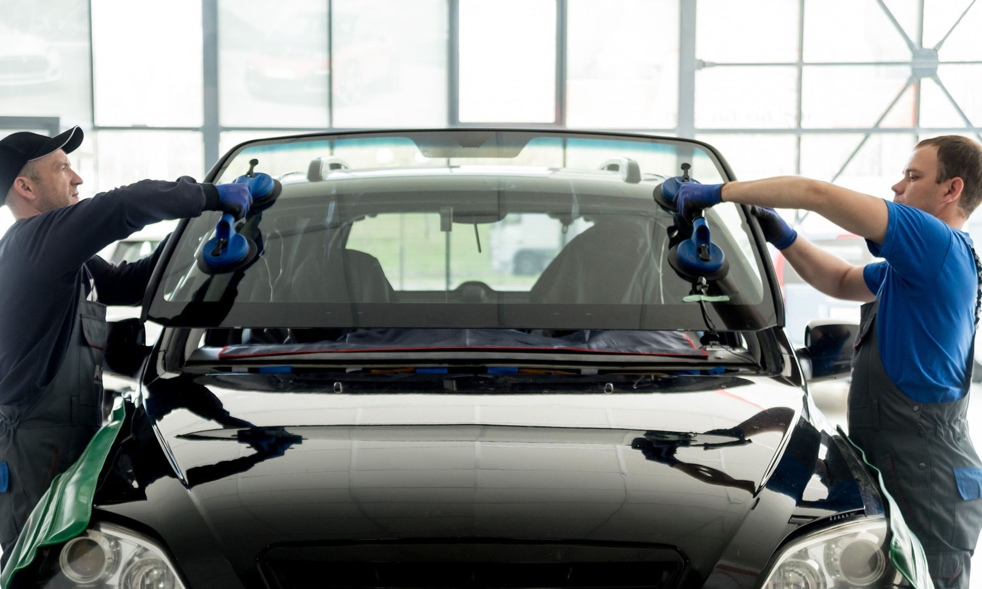 Two workers polishing a black car windshield in an auto shop