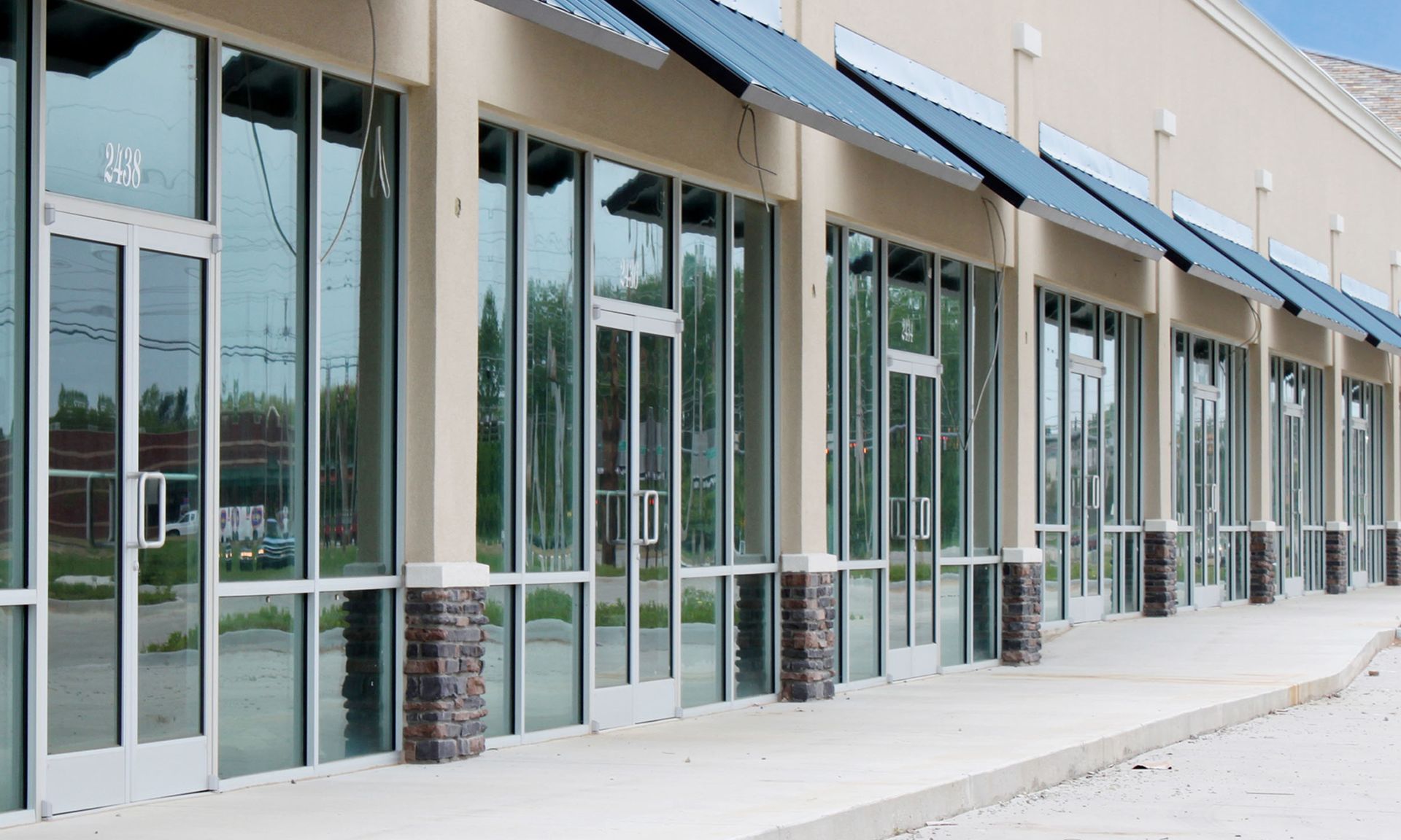 Row of empty storefronts with glass doors and blue awnings along a sidewalk