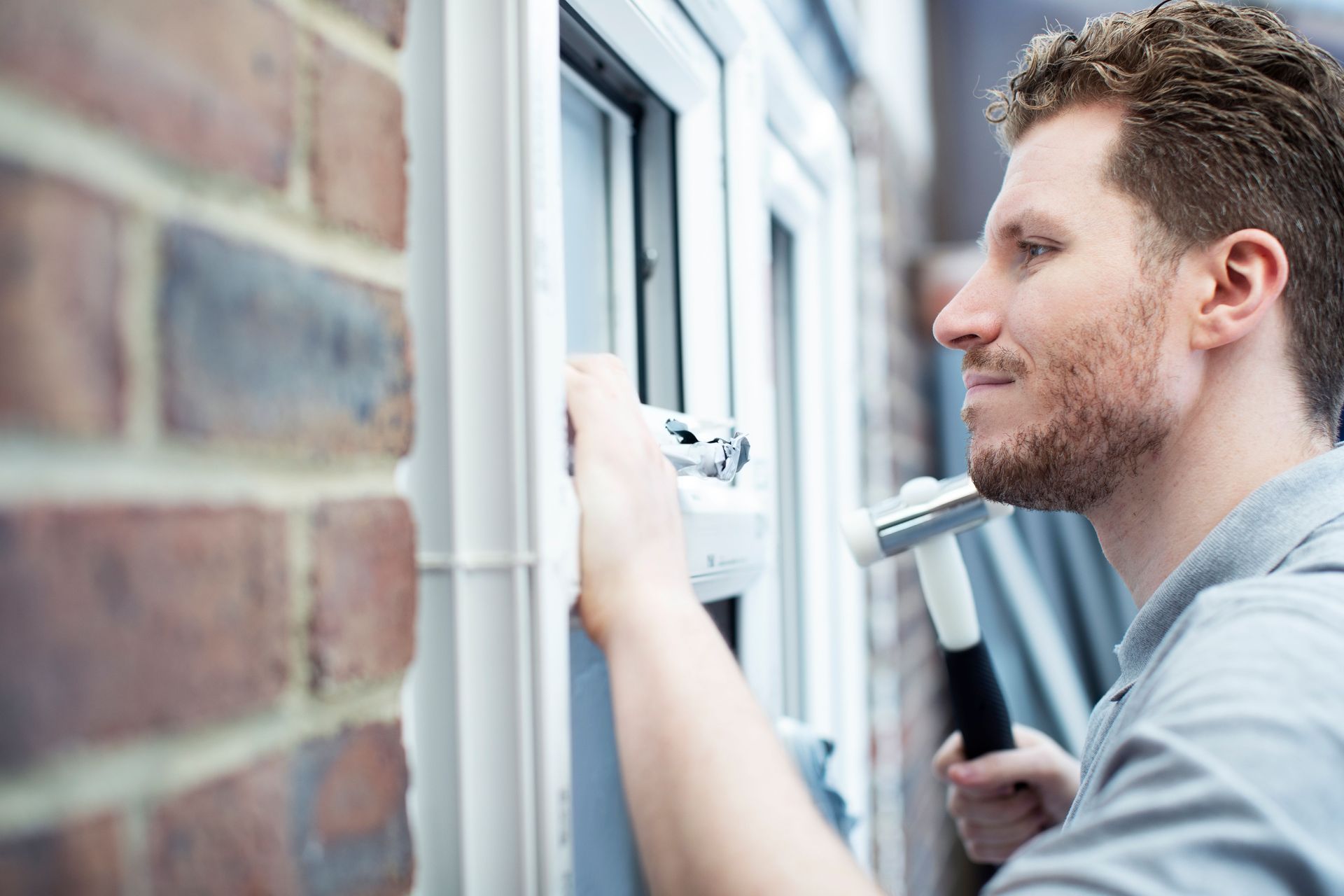 Man painting a window frame beside a brick wall, using a paintbrush and paint roller