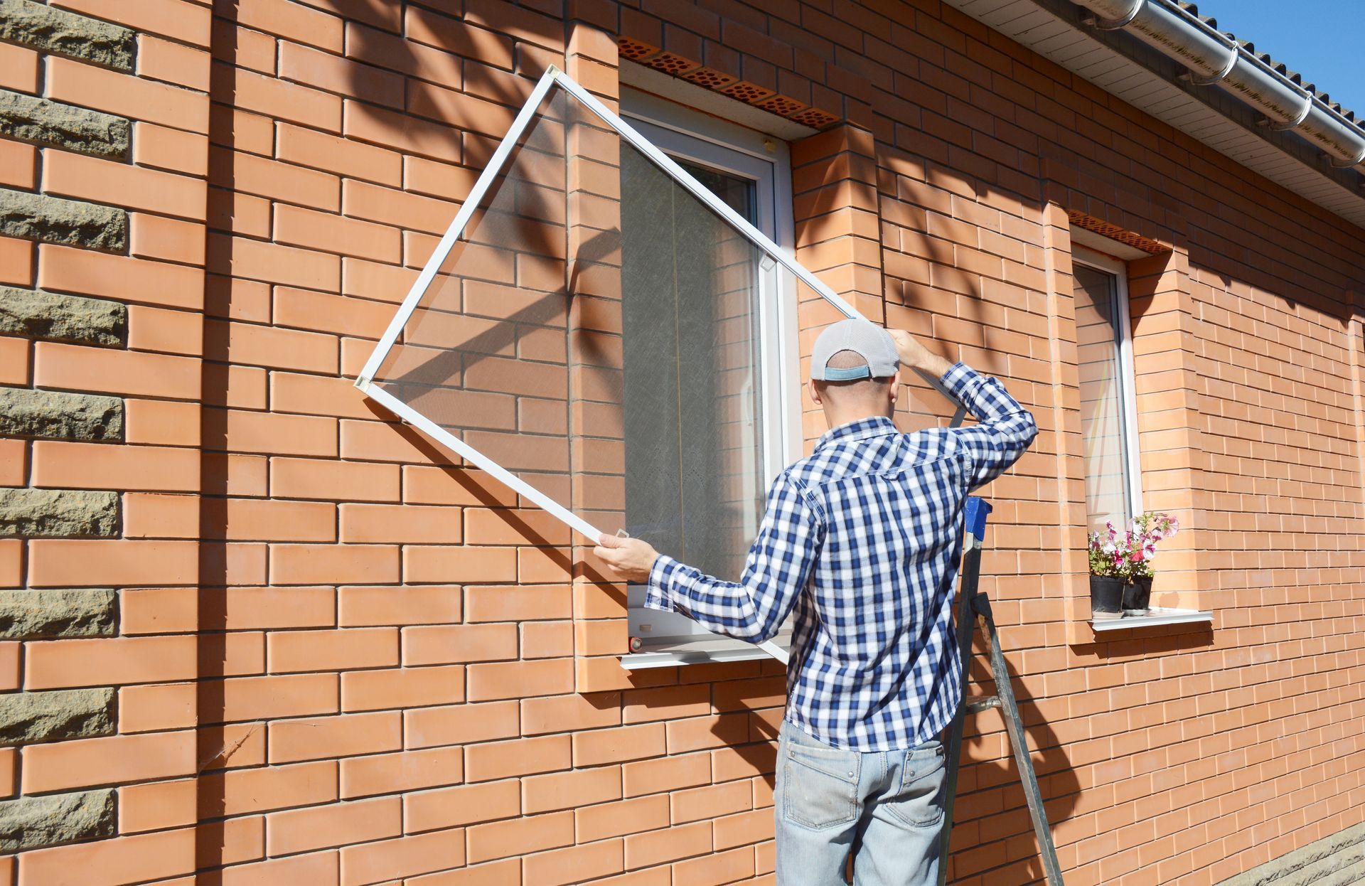 Man installing a window screen on a brick house wall