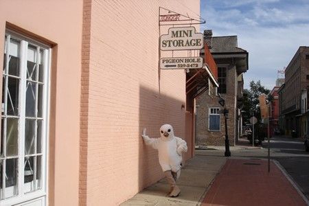 A mascot is standing in front of a mini storage sign