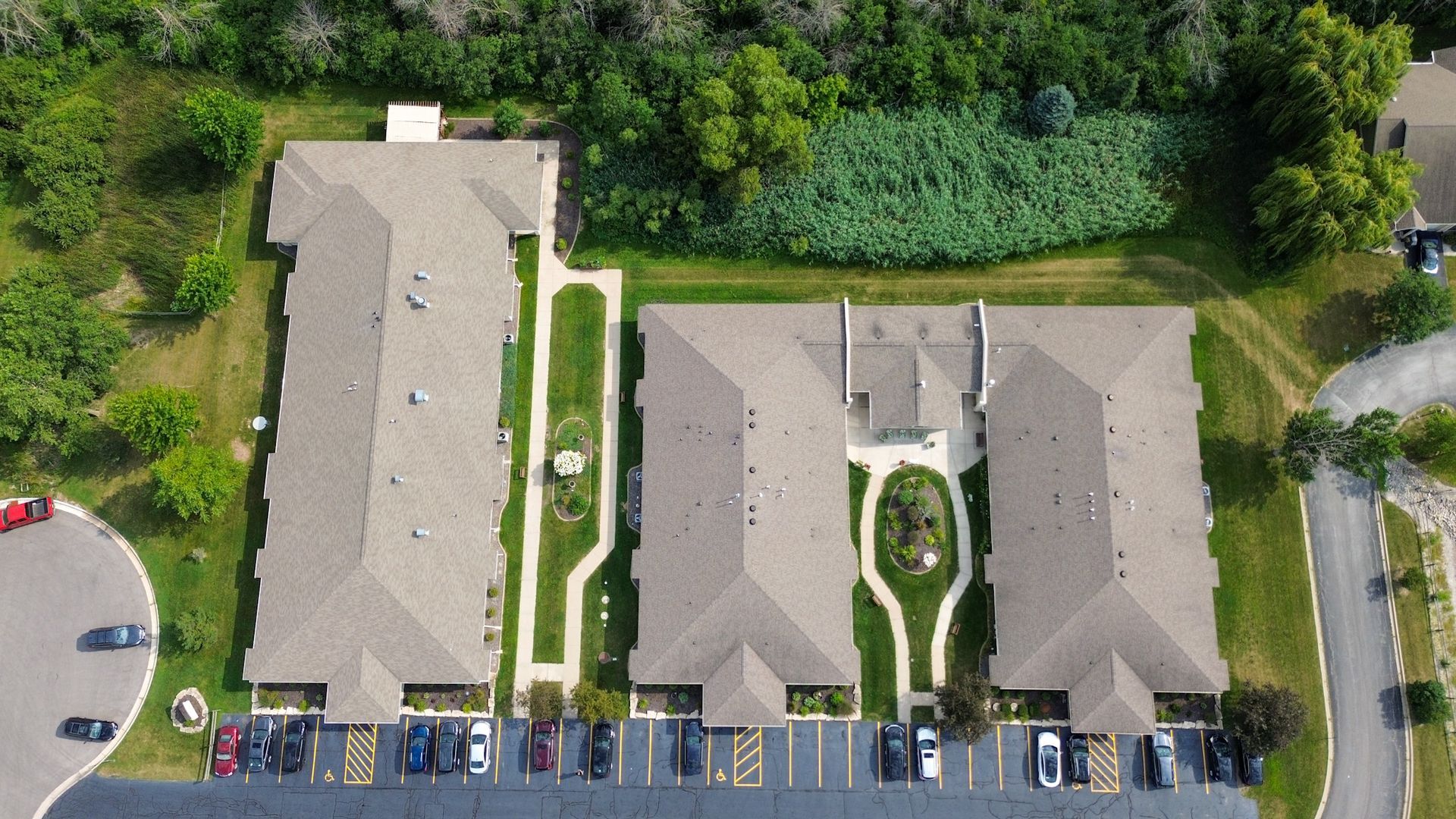 Aerial view of three connected apartment buildings with parking and landscaping.