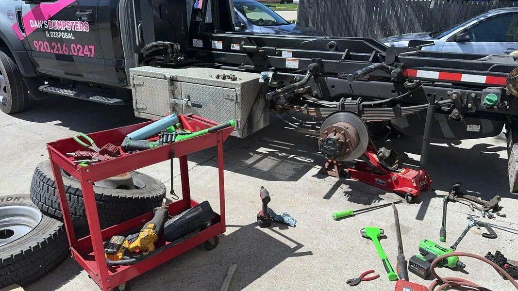 A tow truck is sitting next to a red cart filled with tools.