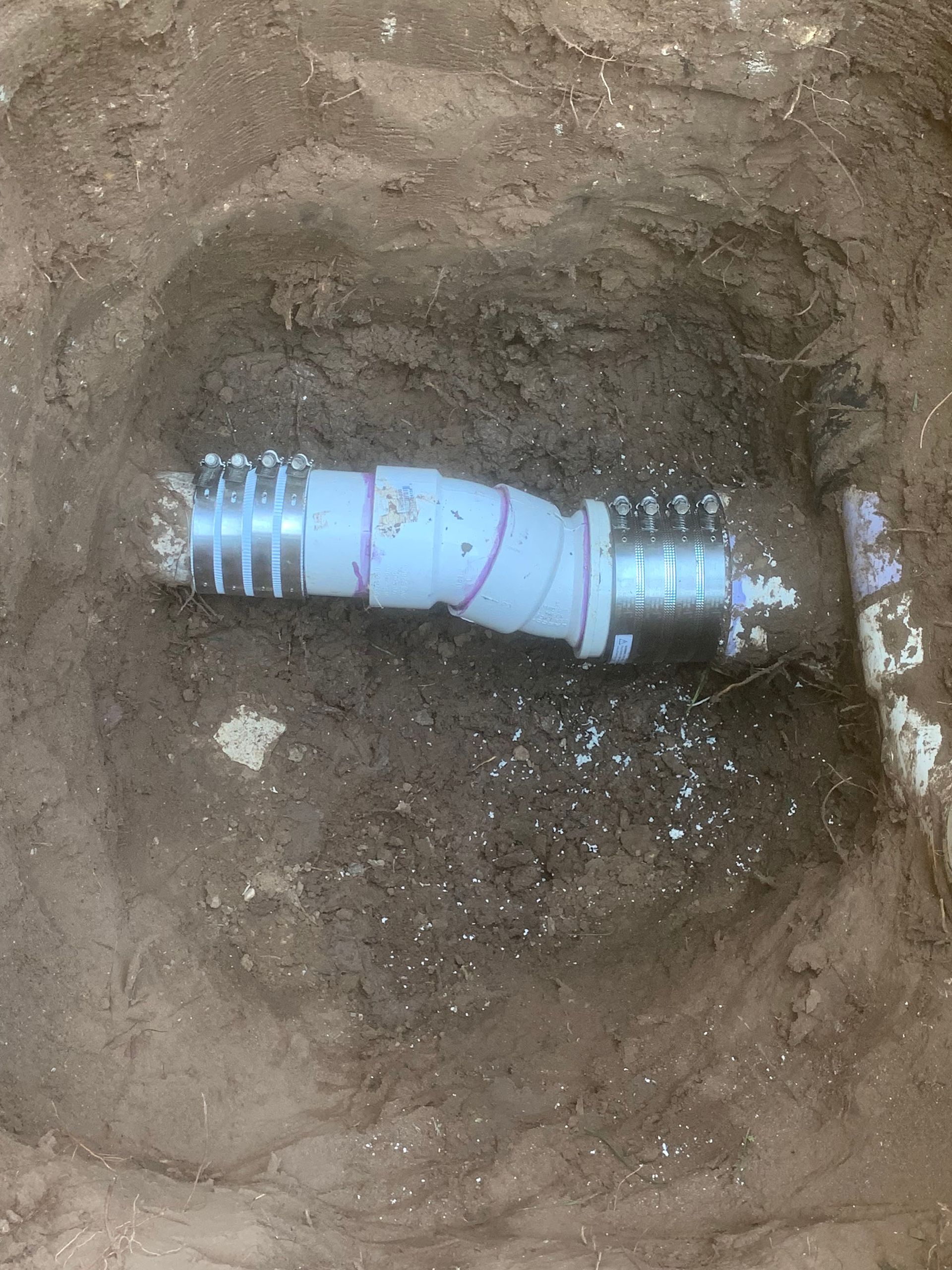 Underground PVC pipe with metal couplings in a dirt hole.
