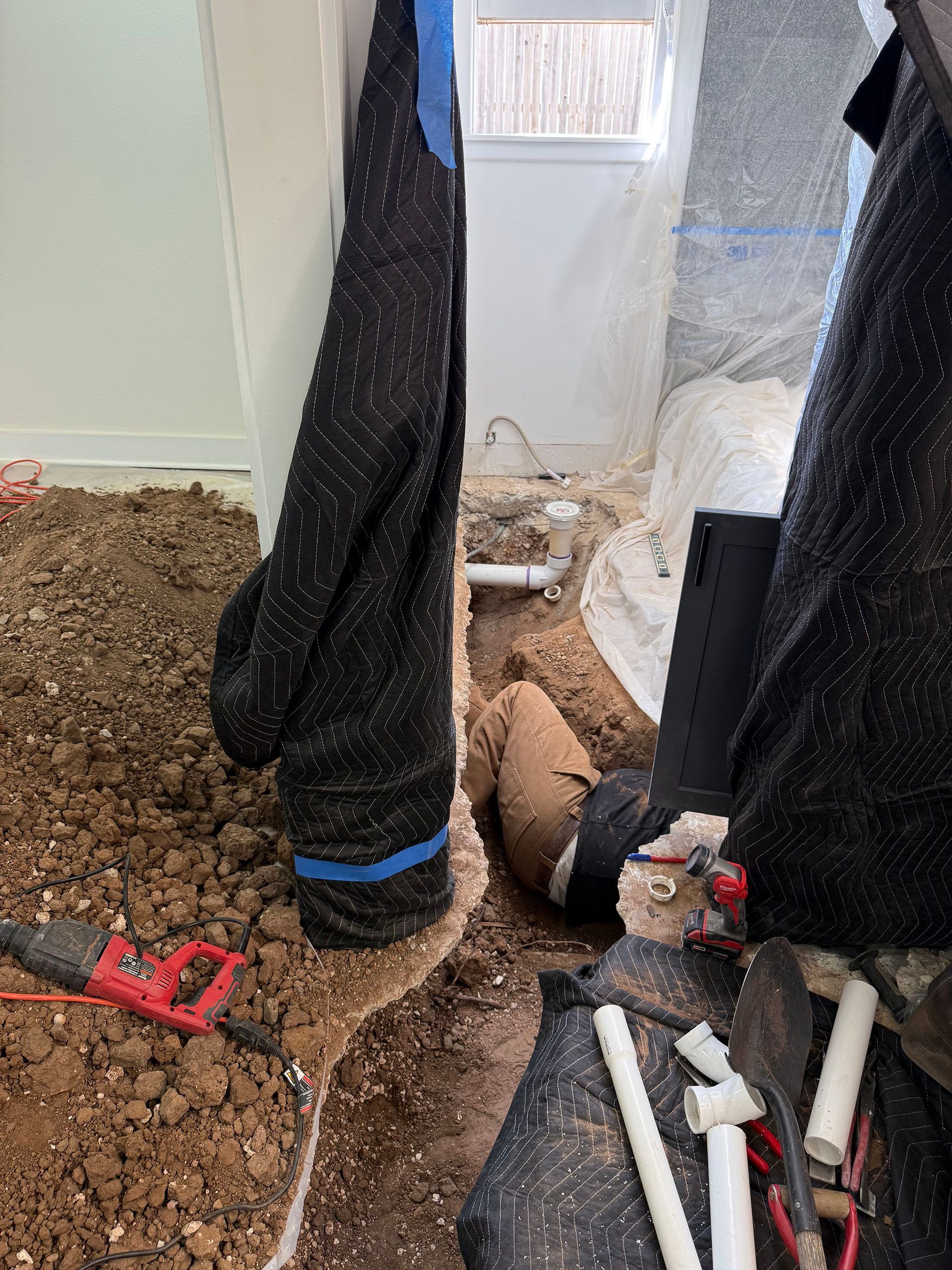 Excavated construction site with exposed pipes. Protective blankets, tools, and dirt are present.