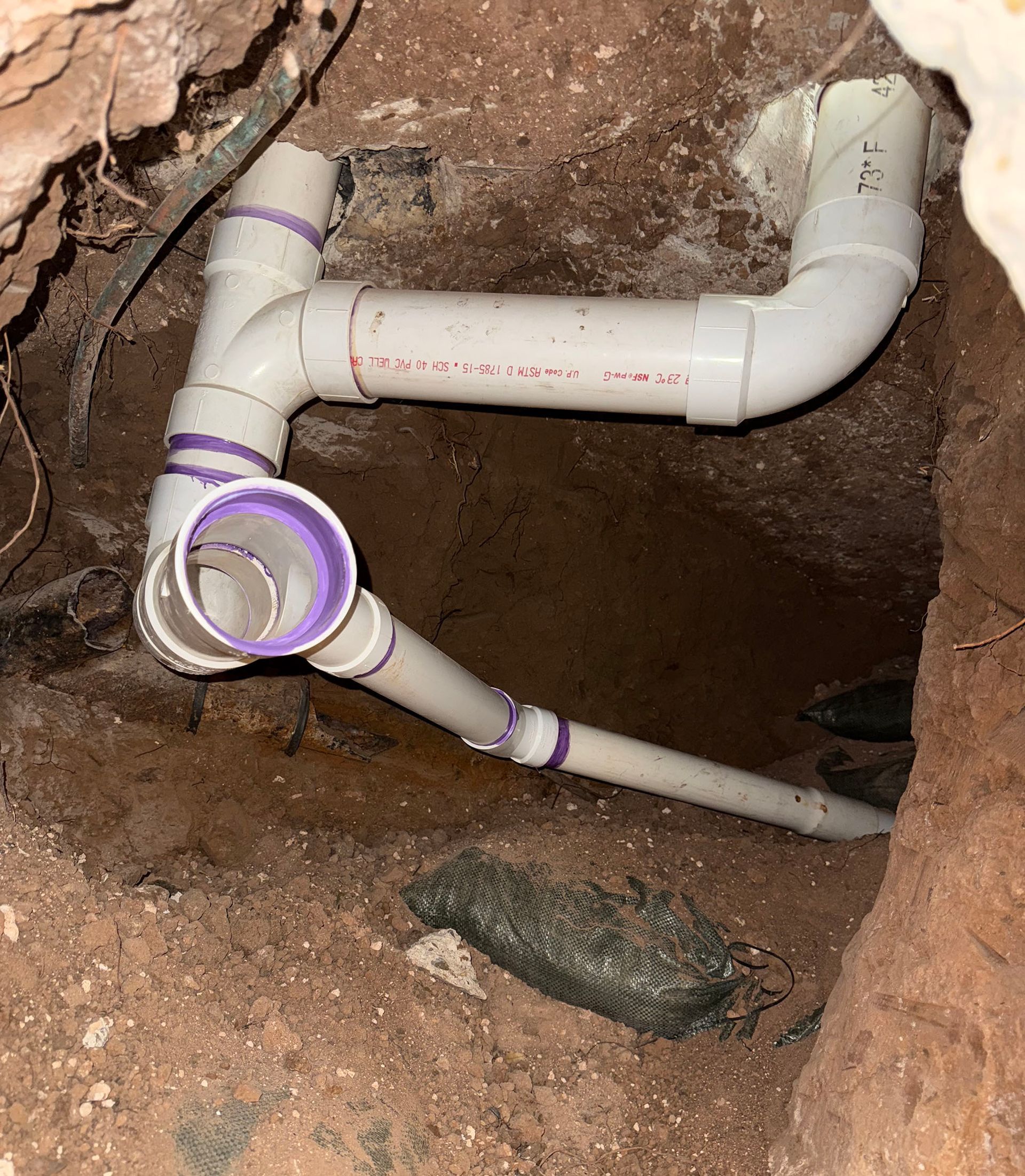White PVC pipes in a dirt hole, forming a plumbing drain system.