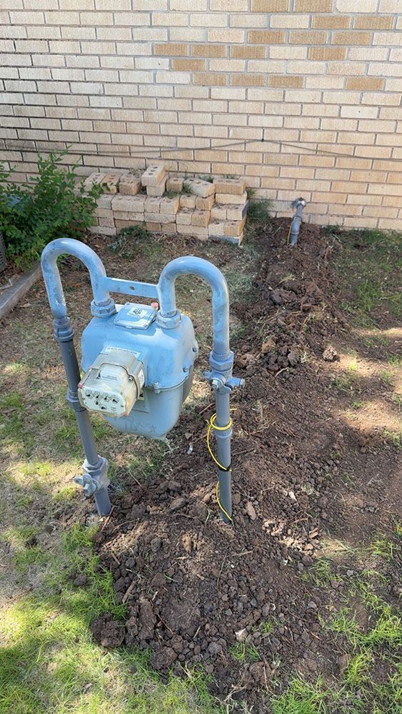 Gas meter and pipes installed near a brick wall and a small patch of grass.