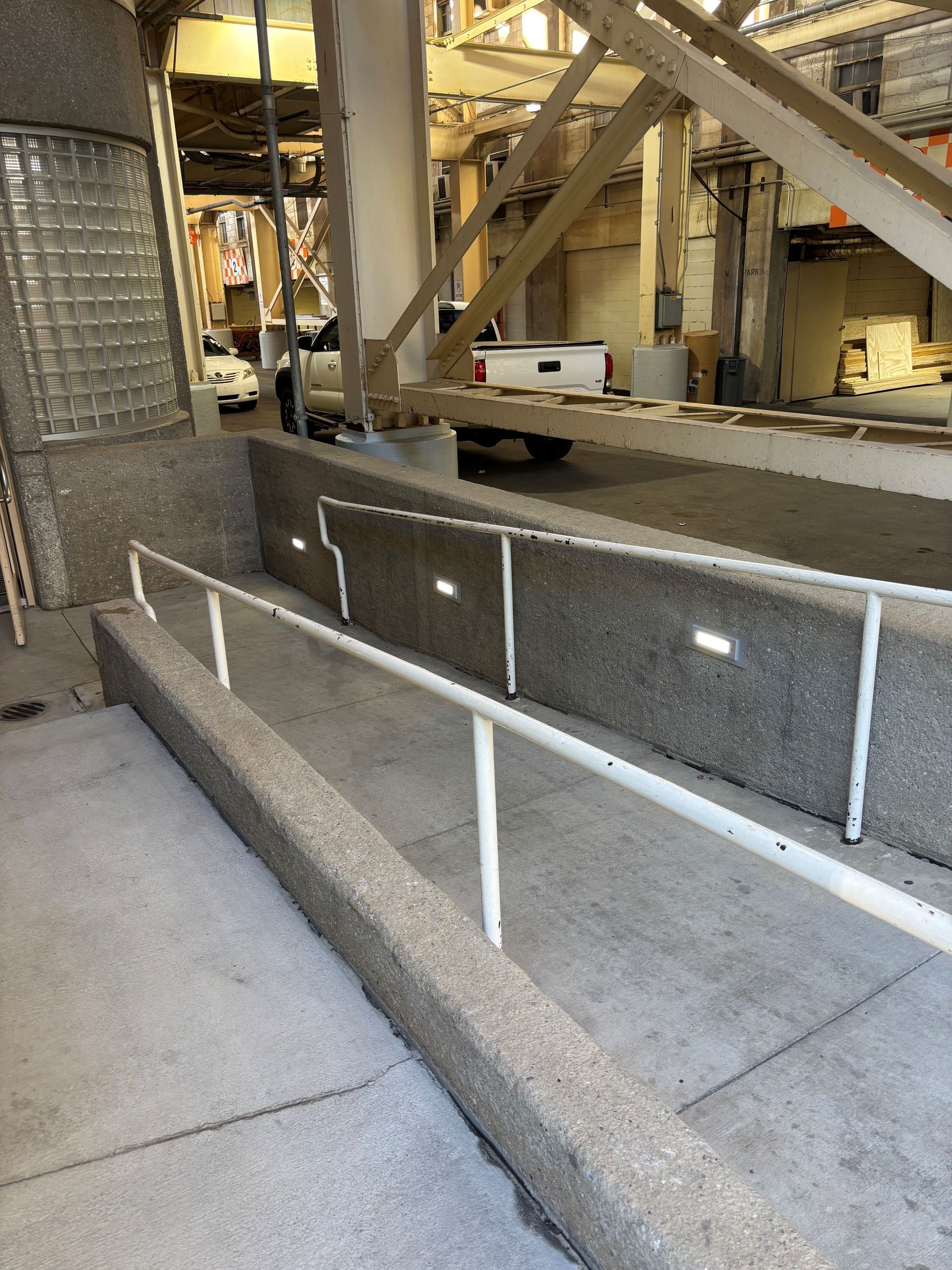 Ramp with white handrails in a building, with grey walls and concrete.
