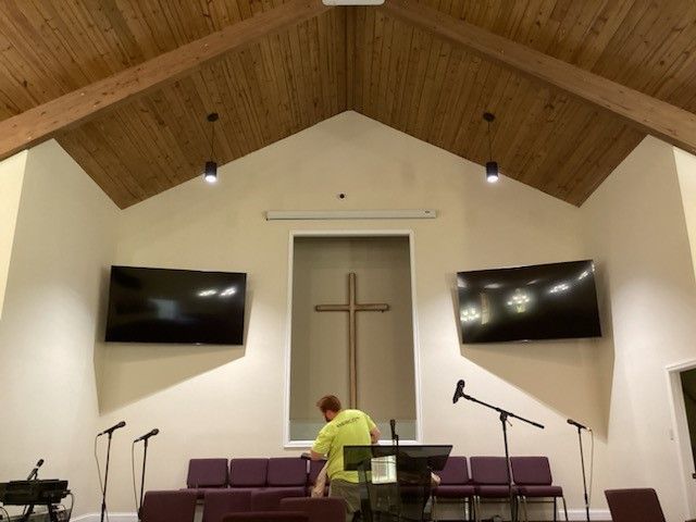 Church interior with cross, screens, and microphones; a person is visible.