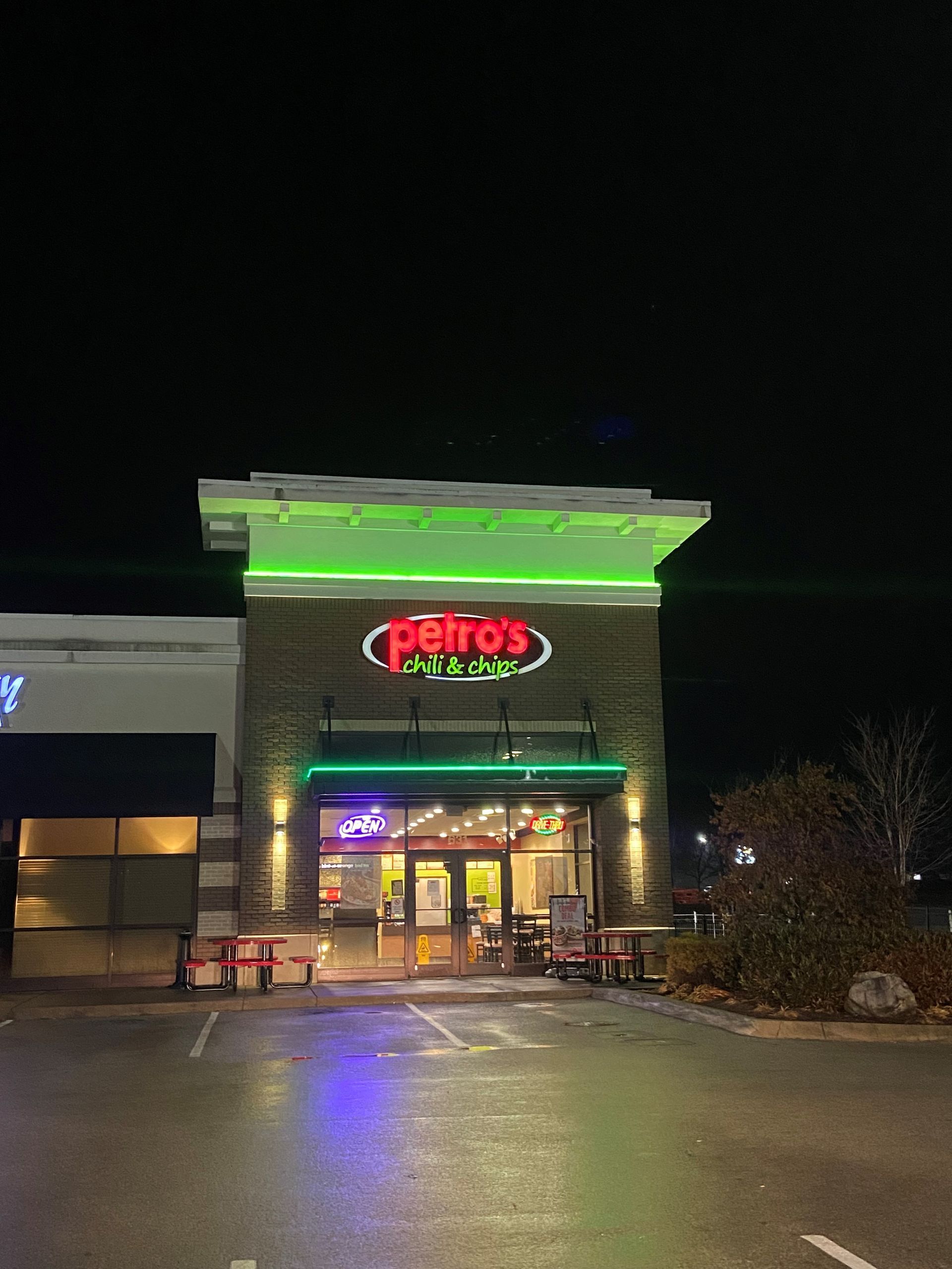 Petro's restaurant at night, green and red neon sign, brick facade, lit entrance, and outdoor seating.