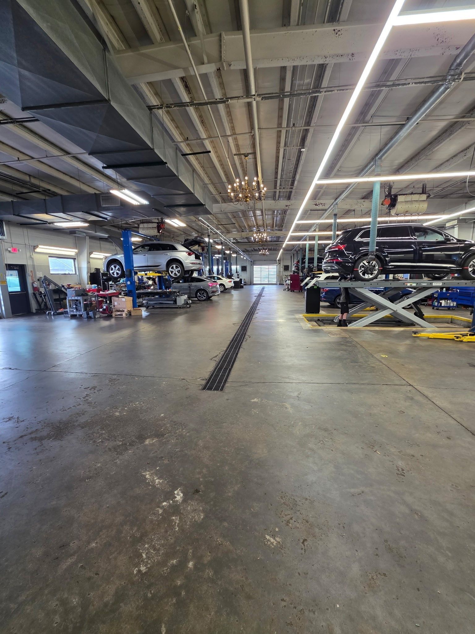 Car repair shop with vehicles on lifts, concrete floor, overhead lighting.