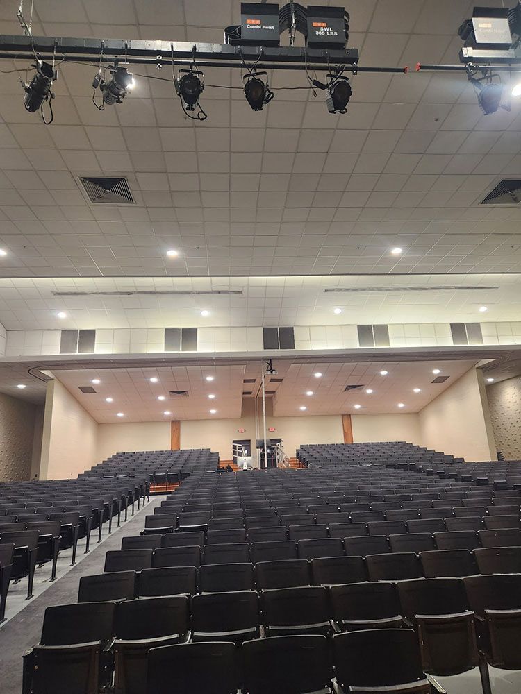 Auditorium with rows of dark seats, stage at the far end, and lighting fixtures overhead