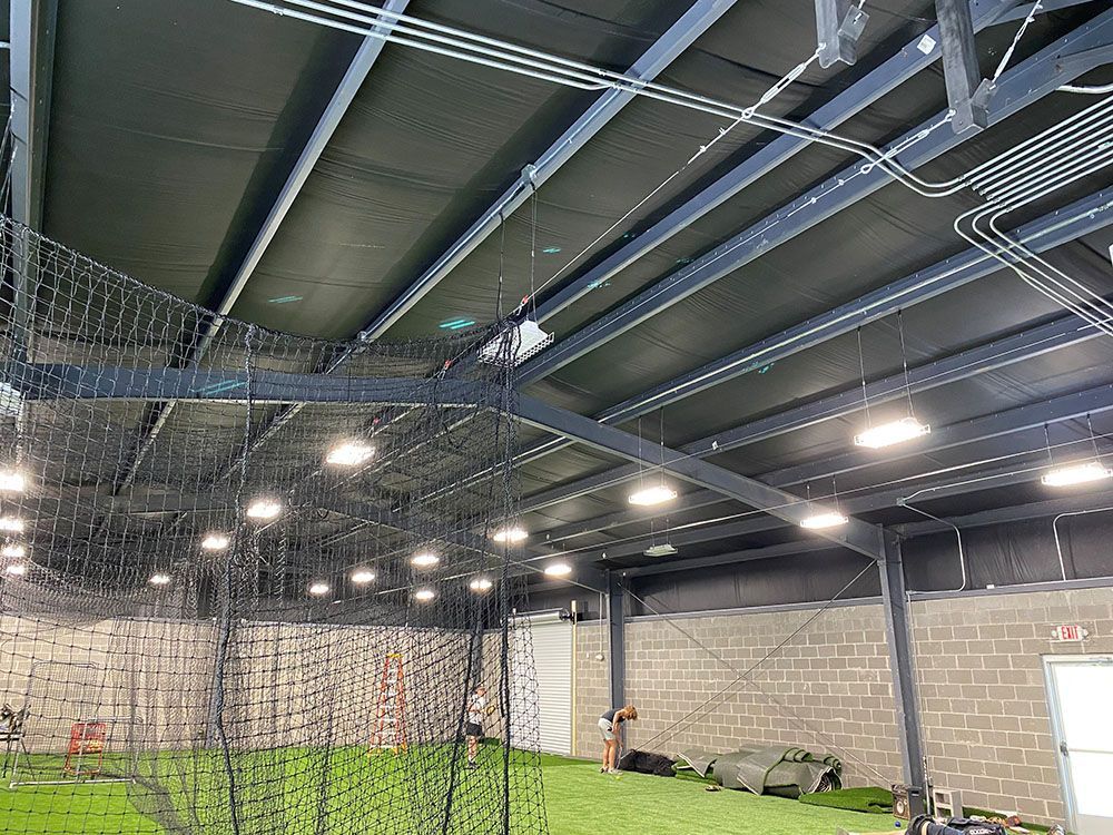 Indoor baseball training facility with netting, turf, and overhead lighting