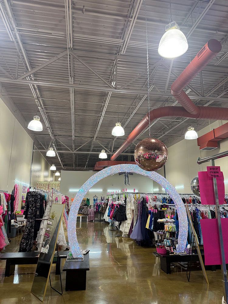 Interior of a brightly lit boutique with a sparkly arch, dresses, and a disco ball hanging from the ceiling