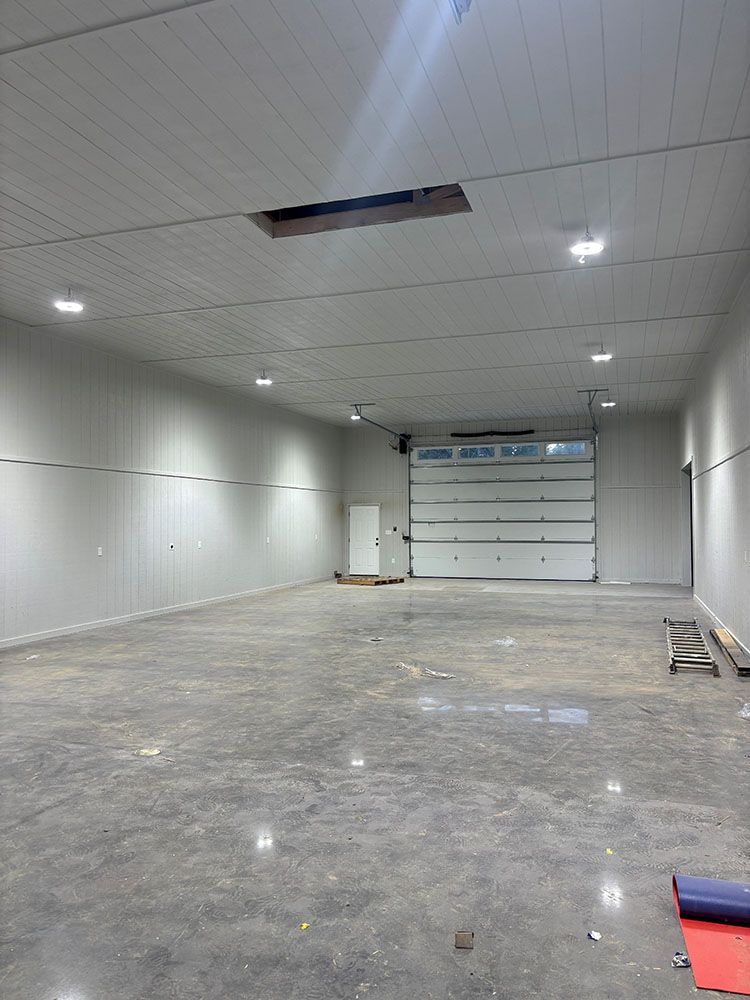 Empty warehouse interior with a large garage door, white walls, and a hole in the ceiling