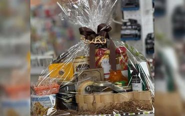 Learn More About Us Gift basket with assorted gourmet foods, wrapped in clear cellophane with a brown ribbon bow.