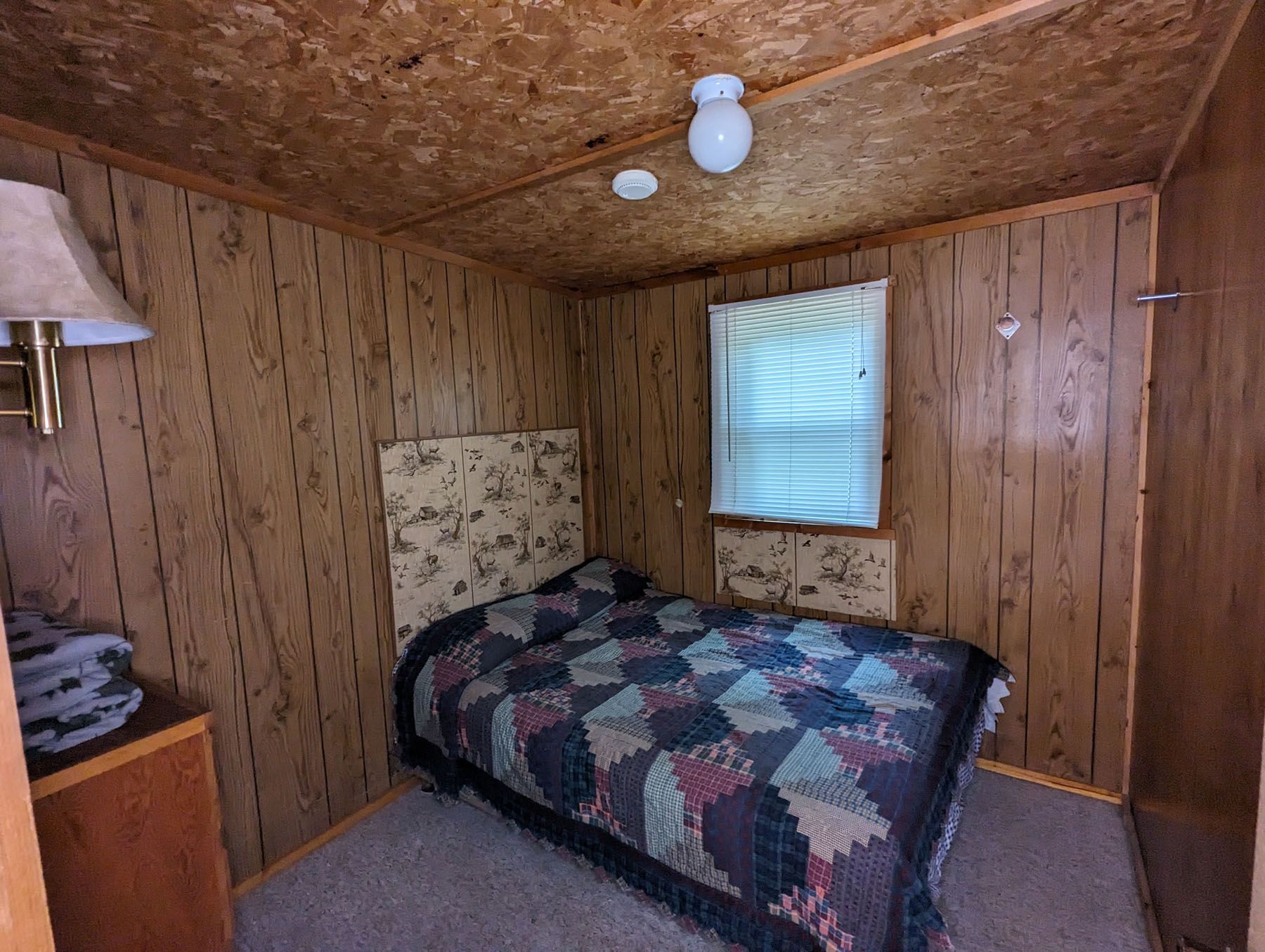 a bedroom with a bed, dresser, lamp and window