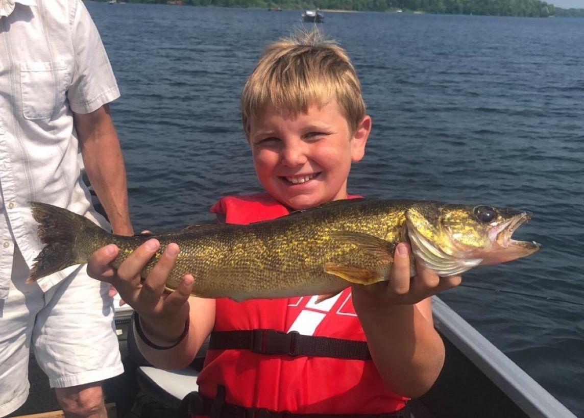 a young boy in a life jacket is holding a fish