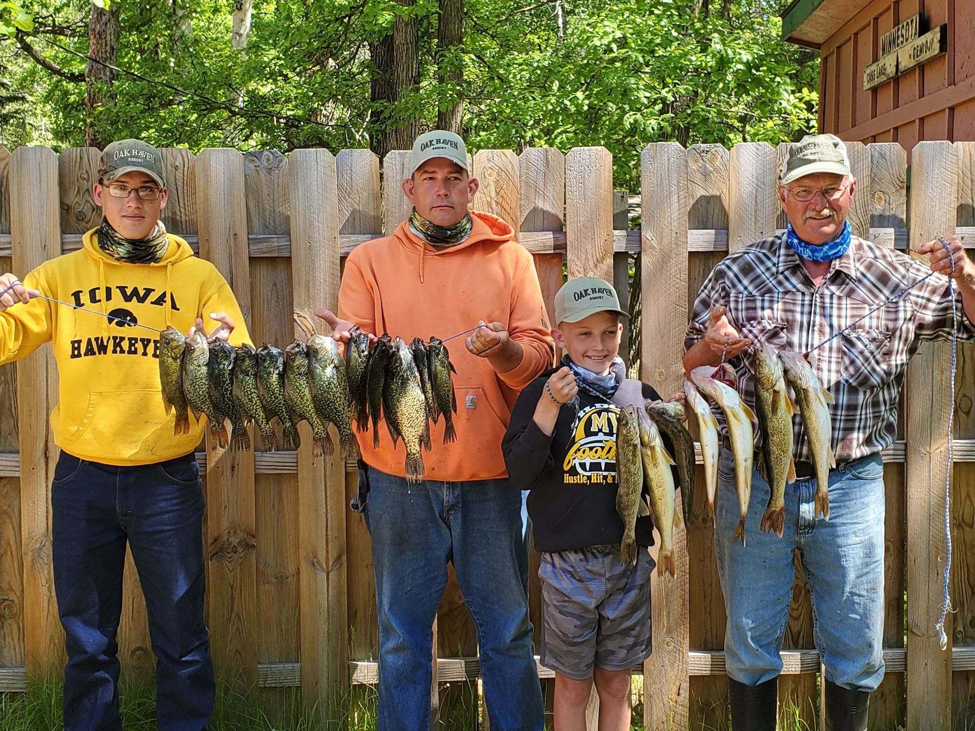 a group of men standing next to each other holding fish in front of a wooden fence .
