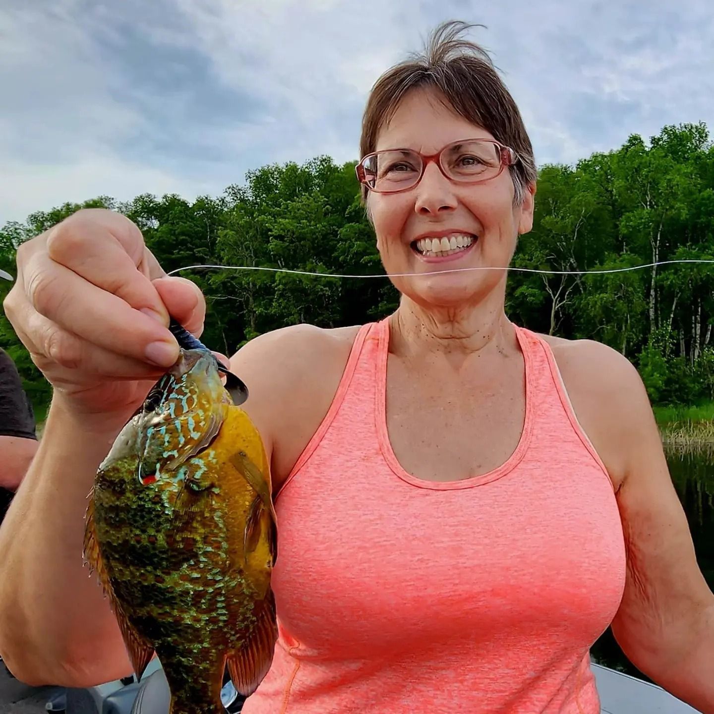 a woman in a pink tank top is holding a fish in her hand .