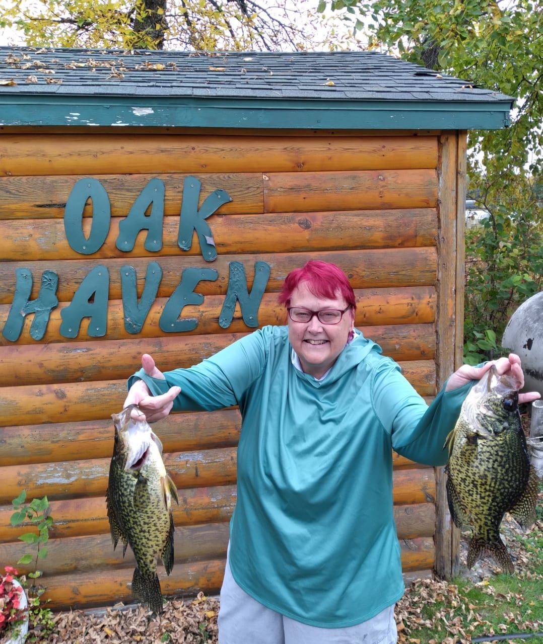 a woman is holding two fish in front of a sign that says oak haven