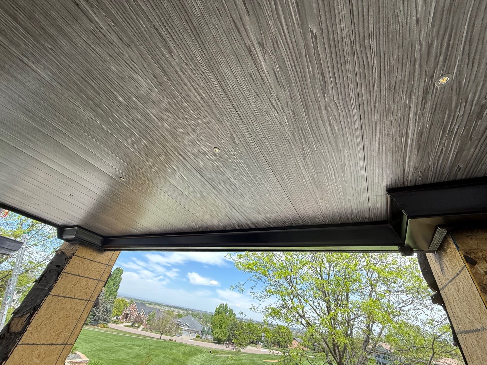 The ceiling of a porch with a view of a lush green field.