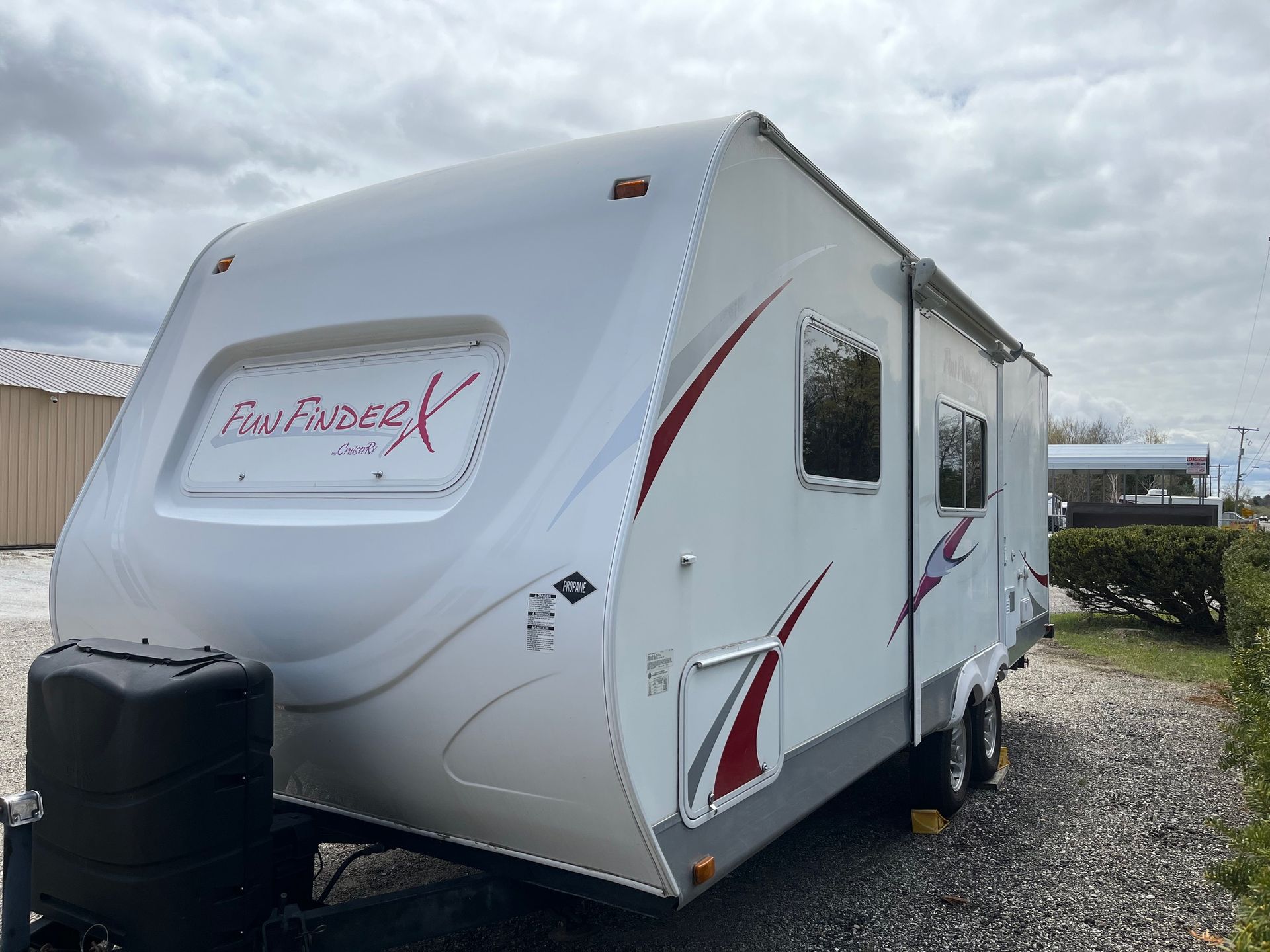 White travel trailer with red graphics parked on a gravel lot under a cloudy sky