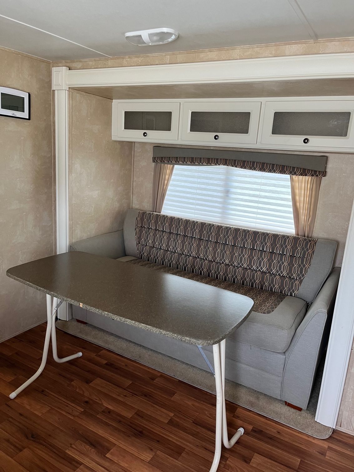 Small RV dinette with gray bench seating, fold-down table, and patterned cushions under cabinets.